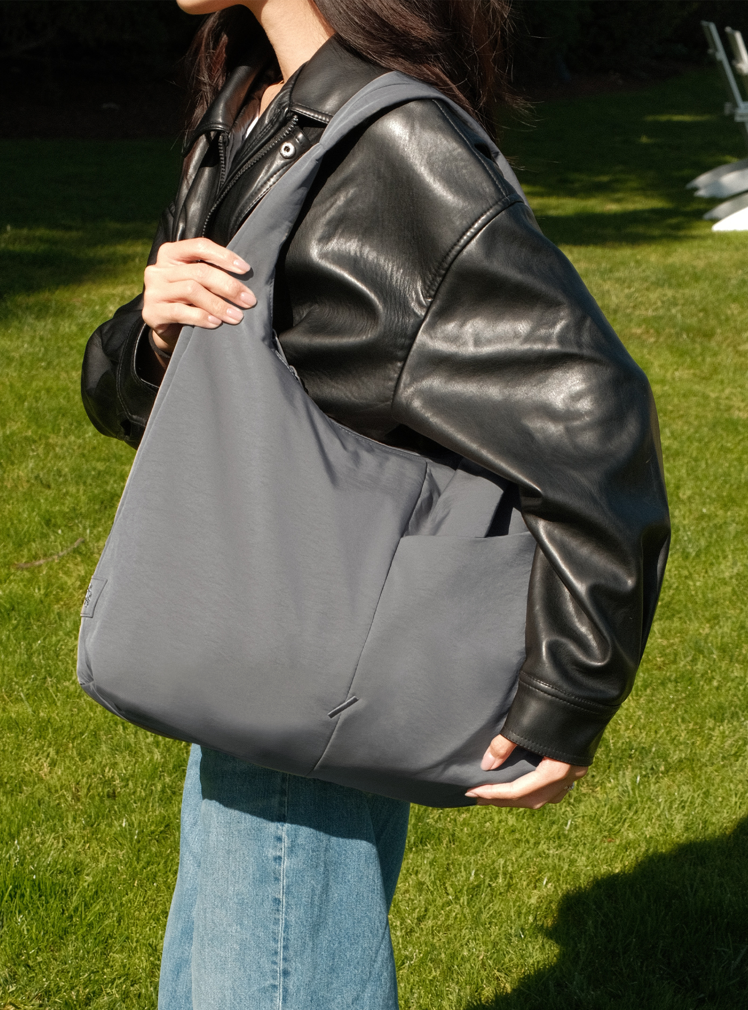 Woman holding the Arc slouchy hobo-style bag in grey nylon for work and travel