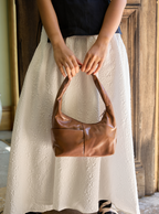 Woman holding the Mini Arc slouchy hobo shoulder bag in warm brown vegan leather