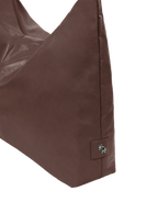 Close-up of the Arc hobo-style bag in dark reddish brown matte vegan leather, showing metal logo emblem